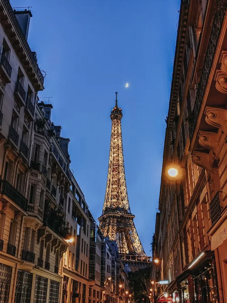 The Eiffel Tower lit up at dusk, seen from a Paris street